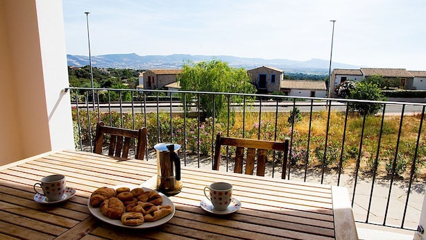 A balcony with a wooden table, two chairs, a plate of pastries, and two cups. - GF Apartments La Vigna - Vigna Garden - SCIROCCO (Badesi)
