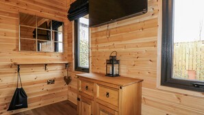 A wooden cabin interior with a wooden cabinet, a mirror, a black lantern, and a TV mounted on the wall. - The Sty (Derby)