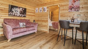 A cozy room with a wooden interior, a pink sofa, a dining table with chairs, and a painting of pigs on the wall. - The Sty (Derby)