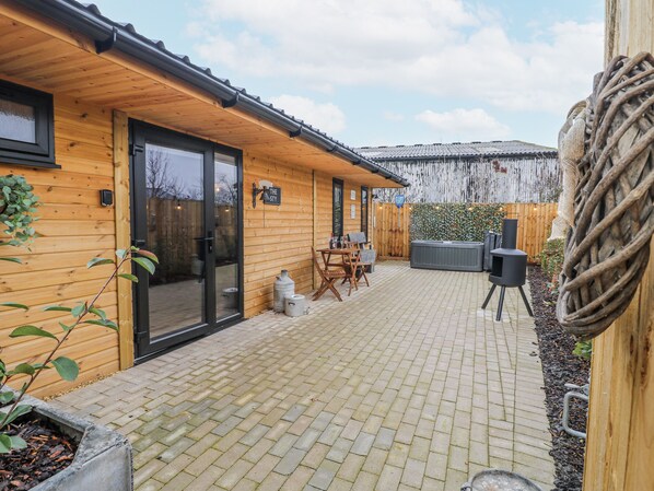 Eine Holzhütte mit Ziegelterrasse, Whirlpool und Grill.