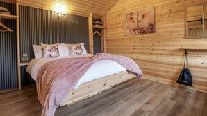A wooden cabin bedroom with a bed, a chandelier, and wooden walls. - The Sty (Derby)