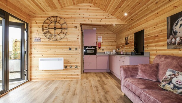 A cozy cabin interior with a wooden ceiling, a kitchen area, and a living space with a pink sofa. - The Sty (Derby)