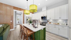 A modern kitchen with white cabinets, a central island, and a dining area with wooden chairs. - Private Pool Home, Sleeps 14, Panama City Beach (Panama City Beach)