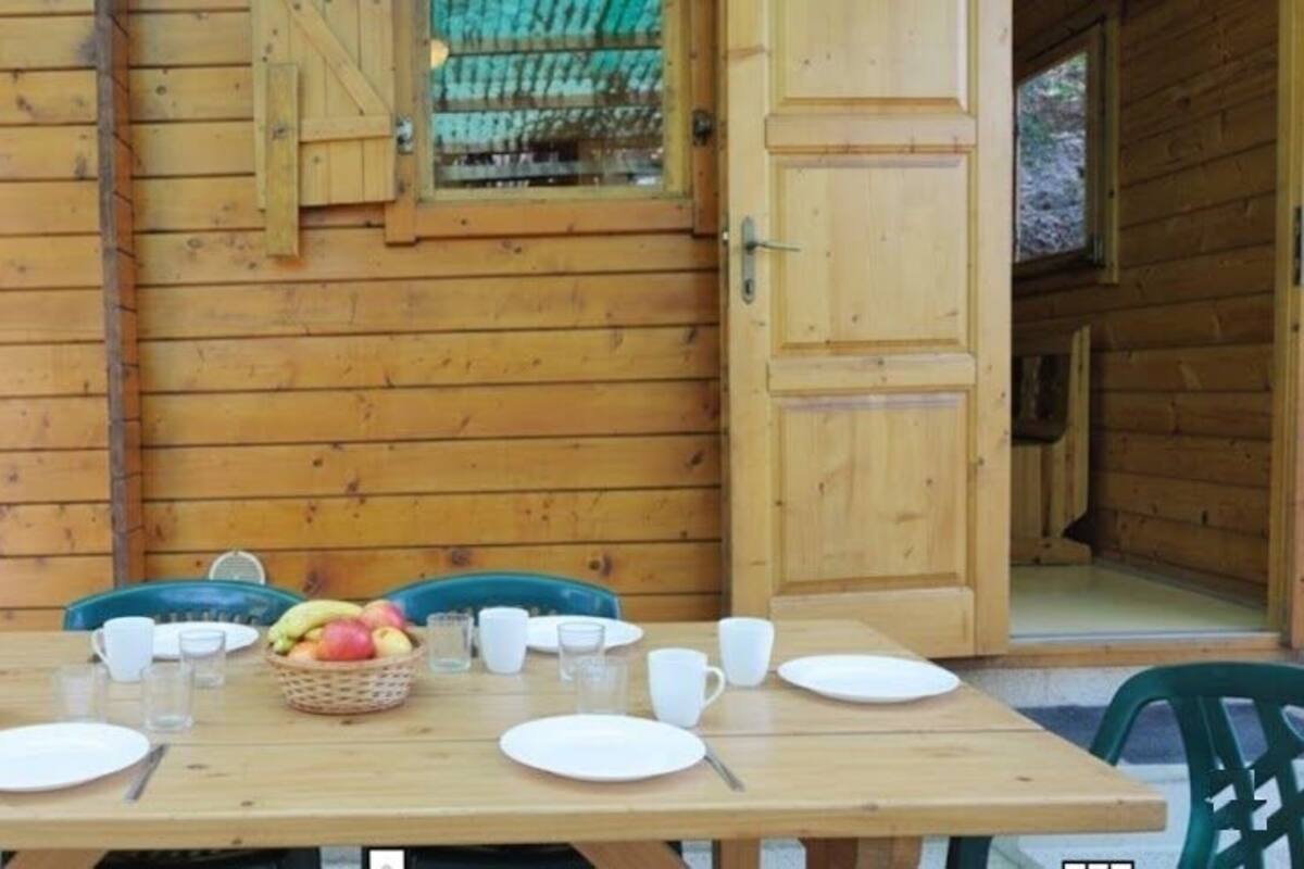 Une table de salle à manger en bois, mise avec des assiettes, des tasses et un panier de fruits.