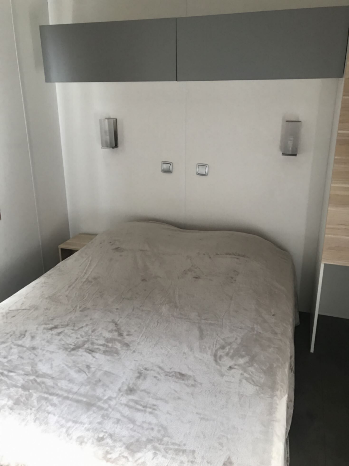 Un lit avec une tête de lit grise et deux appliques murales.