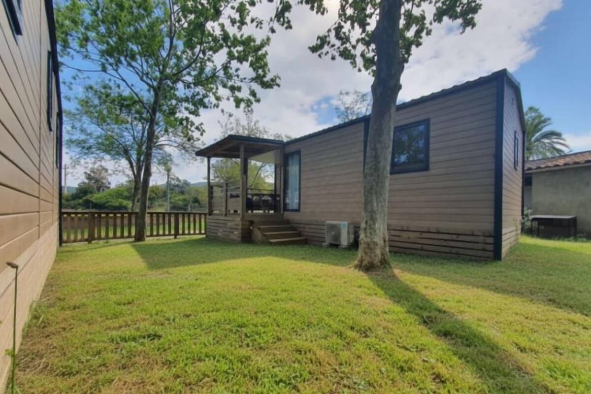 Une petite cabane en bois d’un seul étage, dotée d’un porche couvert, d’une petite terrasse et d’une cour gazonnée.
