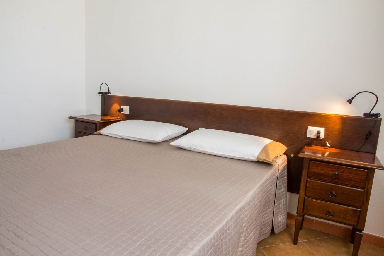 A neatly made bed with a wooden headboard, two bedside tables with lamps, and a small drawer unit.