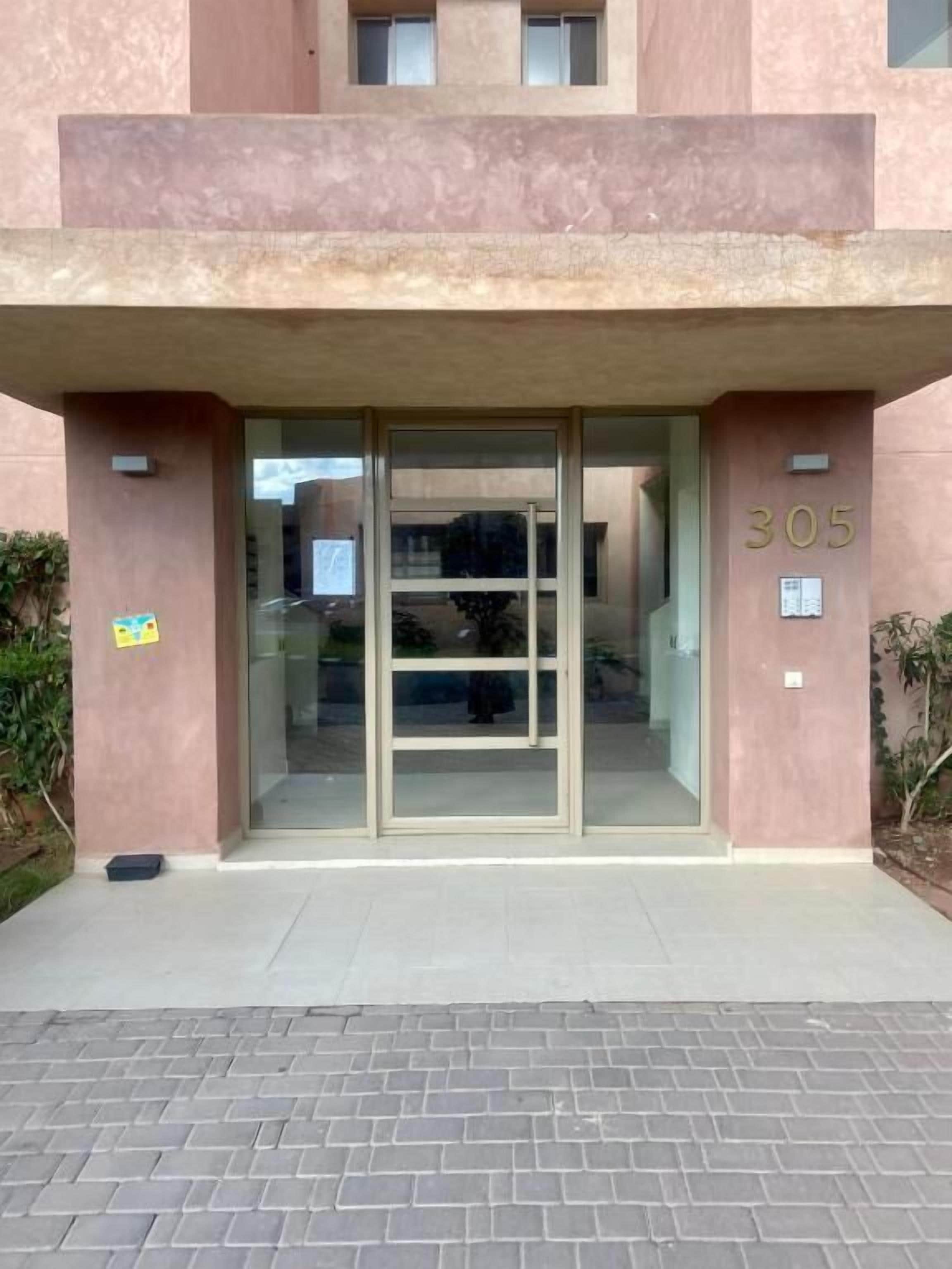 A building entrance with a glass door, a number '305' on the wall, and a paved area in front.
