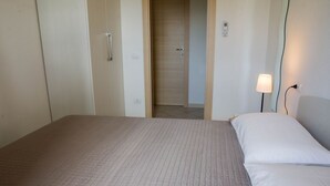 Hotellihuone, jossa on sänky, yöpöytälamppu ja ovi, joka johtaa toiseen huoneeseen.