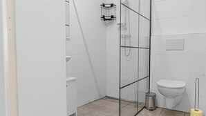 Un baño moderno con cabina de ducha de vidrio, inodoro y un cubo de basura.