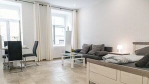 Una habitación de hotel moderna con cama, escritorio, silla, mesa de centro de vidrio y ventana con cortinas.