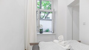 Un dormitorio con cama, ventana con cortinas y vistas a árboles y un edificio.