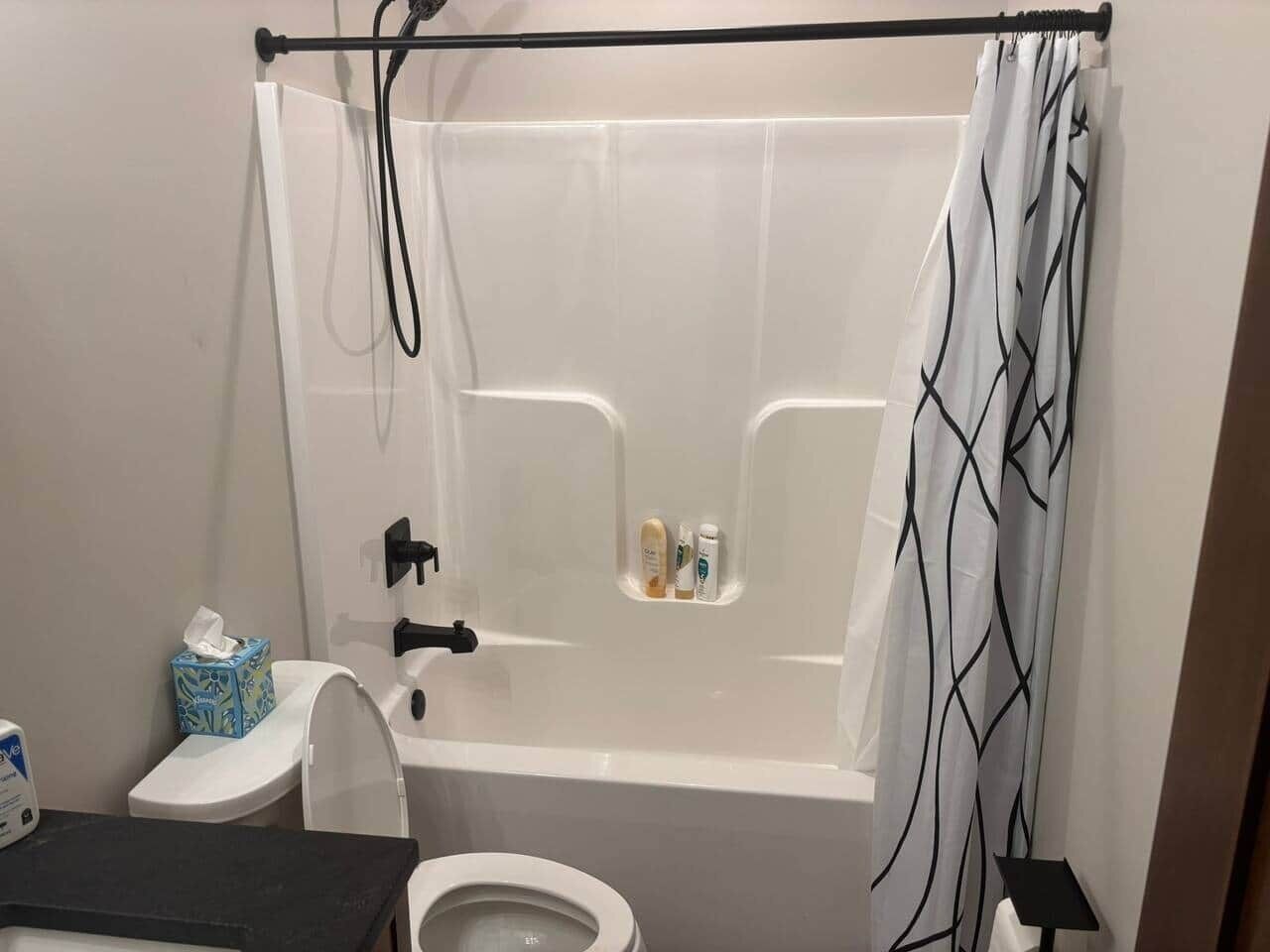 A bathroom with a bathtub, toilet, and a shelf with toiletries.