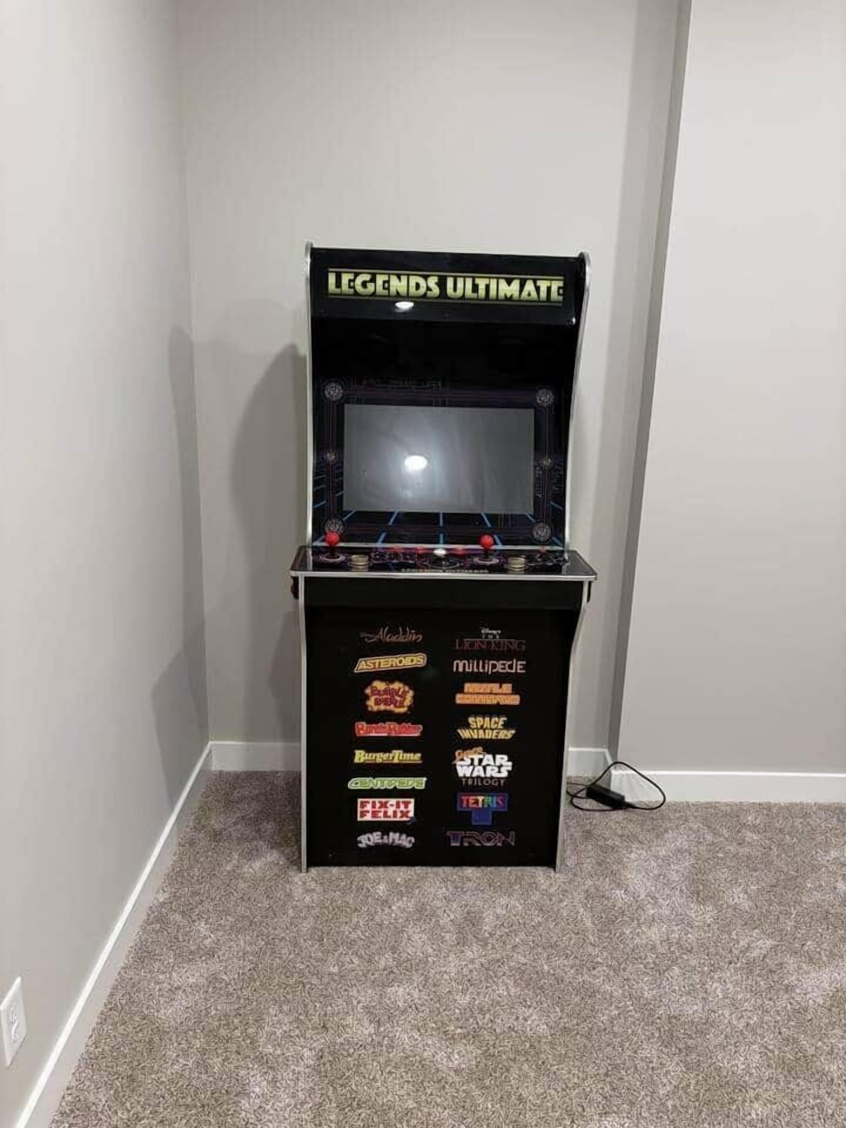 Ein Videospiel-Arcade-Automaten mit der Aufschrift 'LEGENDS ULTIMATE', auf dessen Vorderseite verschiedene Spieloptionen wie 'Asteroids' und 'Space Invaders' angezeigt werden.