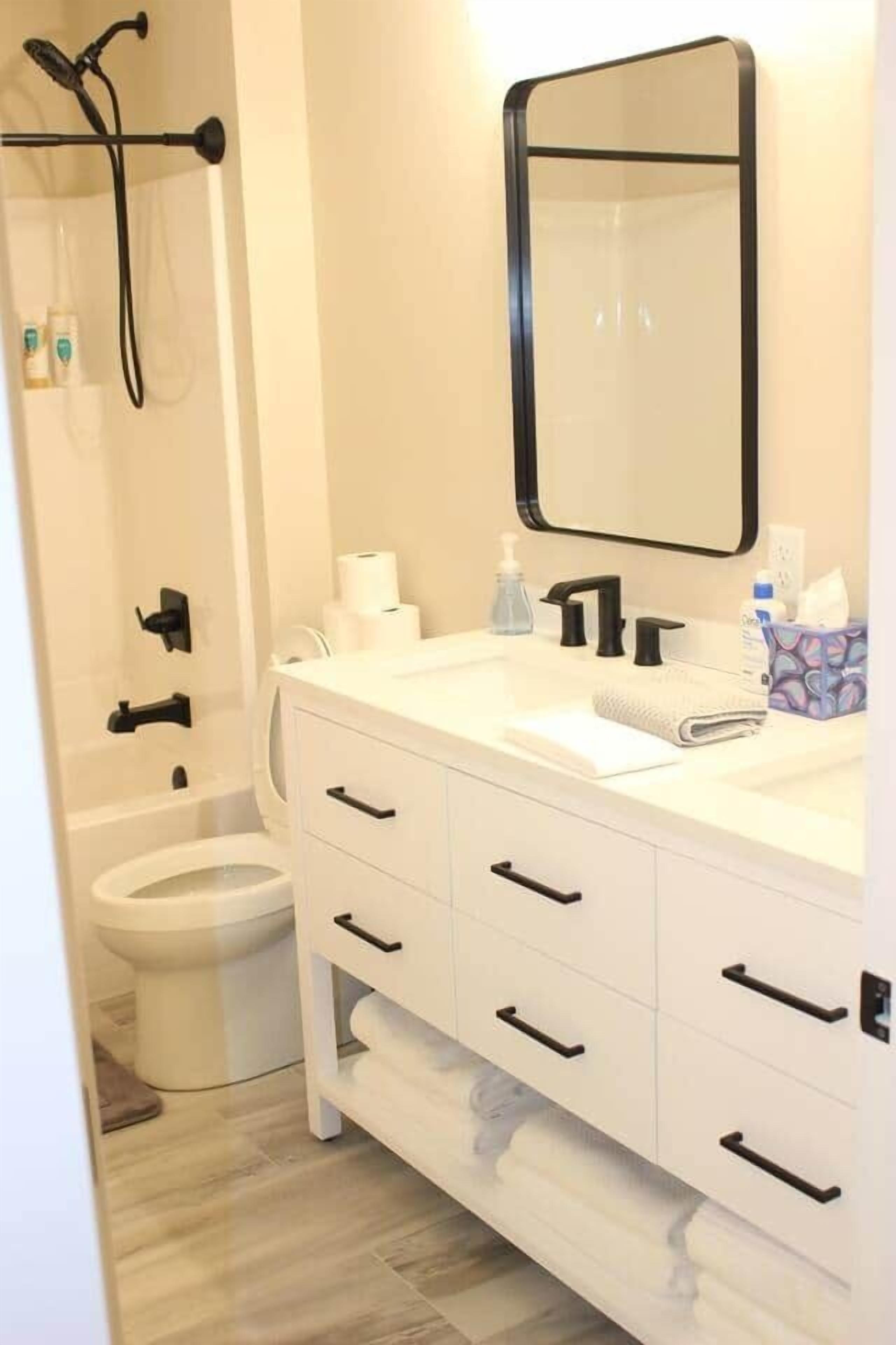 A modern bathroom with a white vanity, a large mirror, a shower area, and a toilet.