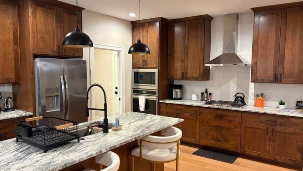 A modern kitchen with wooden cabinets, stainless steel appliances, a marble countertop, and pendant lighting. - Luxurious Sweet Escape stunning custom Home! (Rochester)