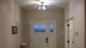 A hallway with wooden flooring, a double door with frosted glass panels, a bench, and a small table with flowers. - Luxurious Sweet Escape stunning custom Home! (Rochester)