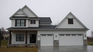 A two-story house with a front porch, a garage, and a driveway. - Luxurious Sweet Escape stunning custom Home! (Rochester)