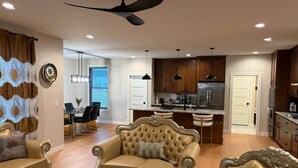 A spacious living room with a large sofa, a coffee table, and a dining area in the background. - Luxurious Sweet Escape stunning custom Home! (Rochester)