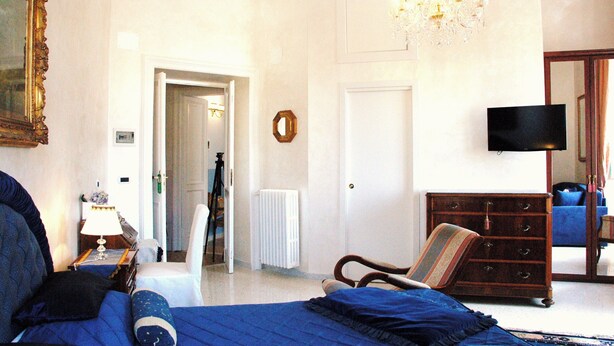 A room with a bed, a dresser, a television, and a chandelier. - Ch Colosseum home (Rome)