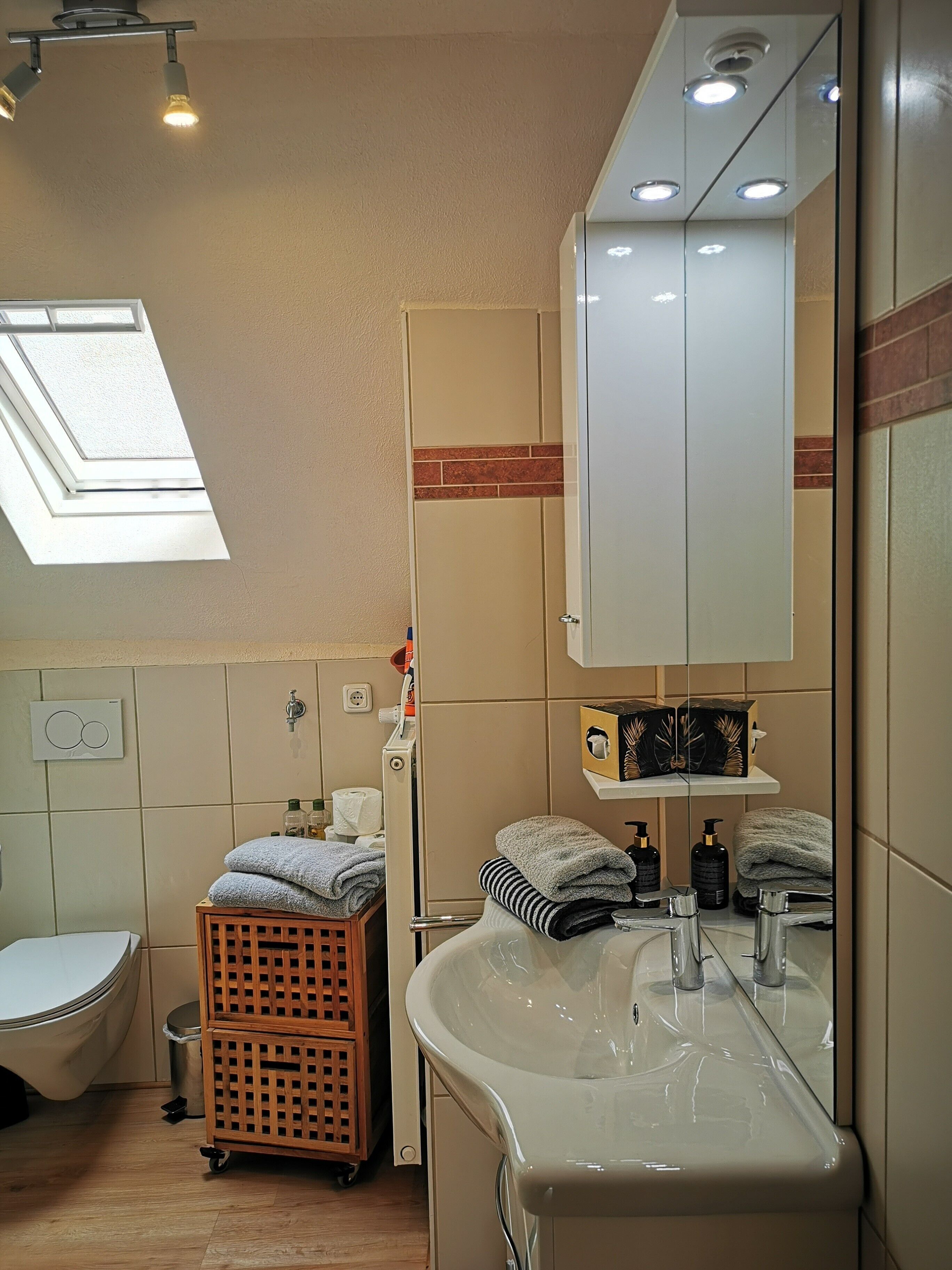 Et badeværelse med ovenlys, badekar, vaskemøbel med spejl og toilet.