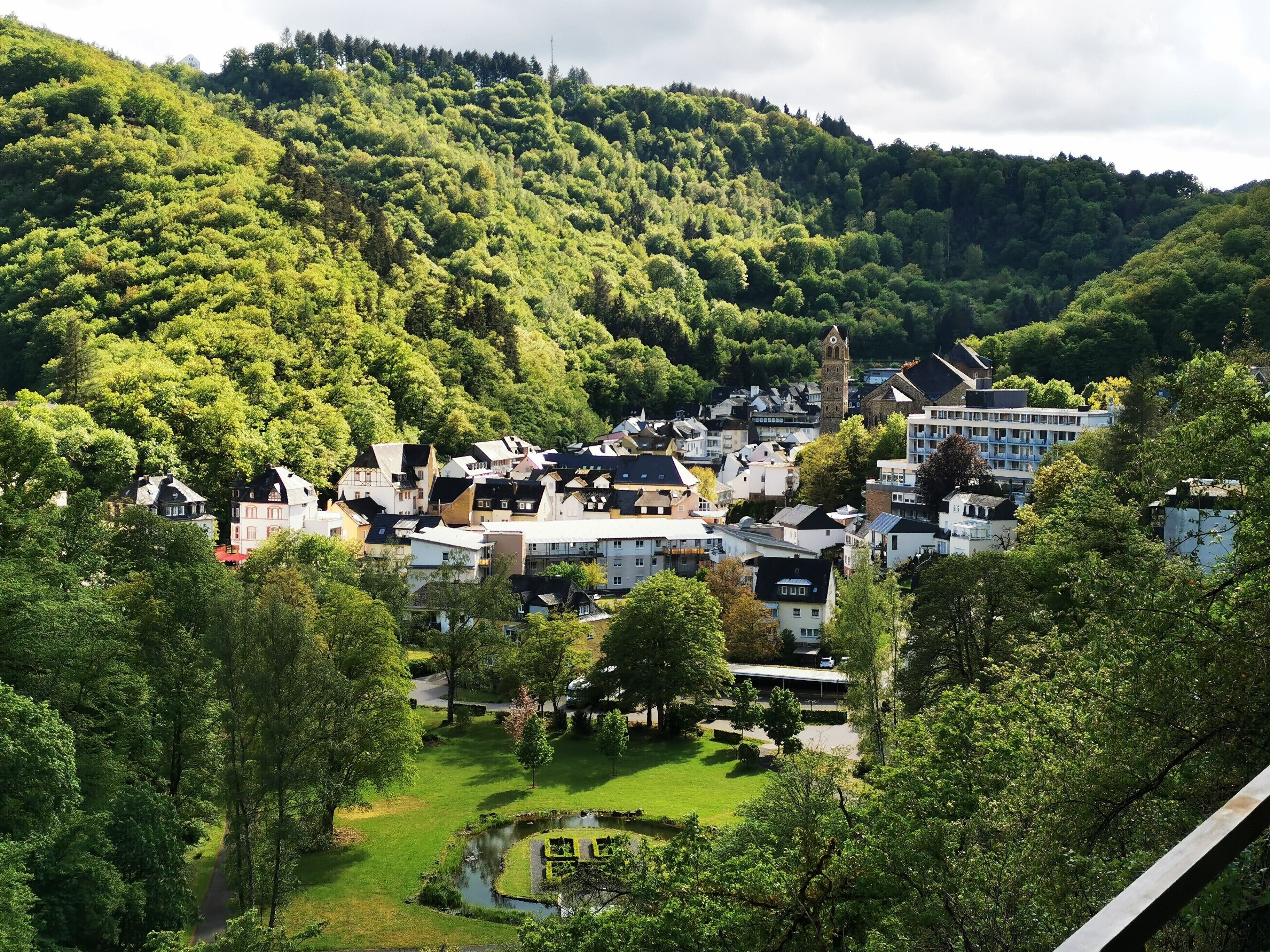 A town with historic buildings, a central square, and a hill with dense forest.