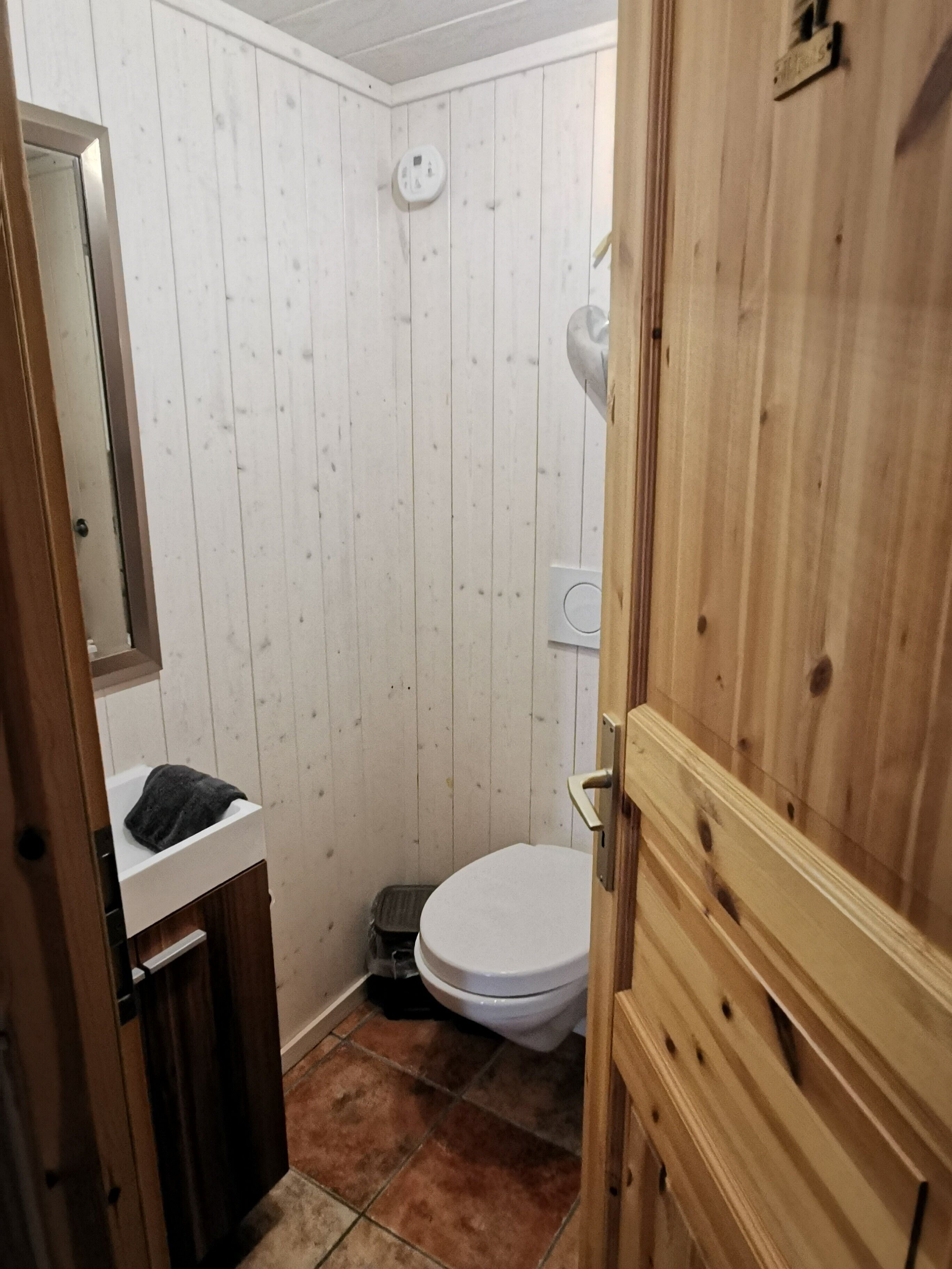 Une petite salle de bain avec des toilettes blanches, un lavabo avec un miroir et une douche.