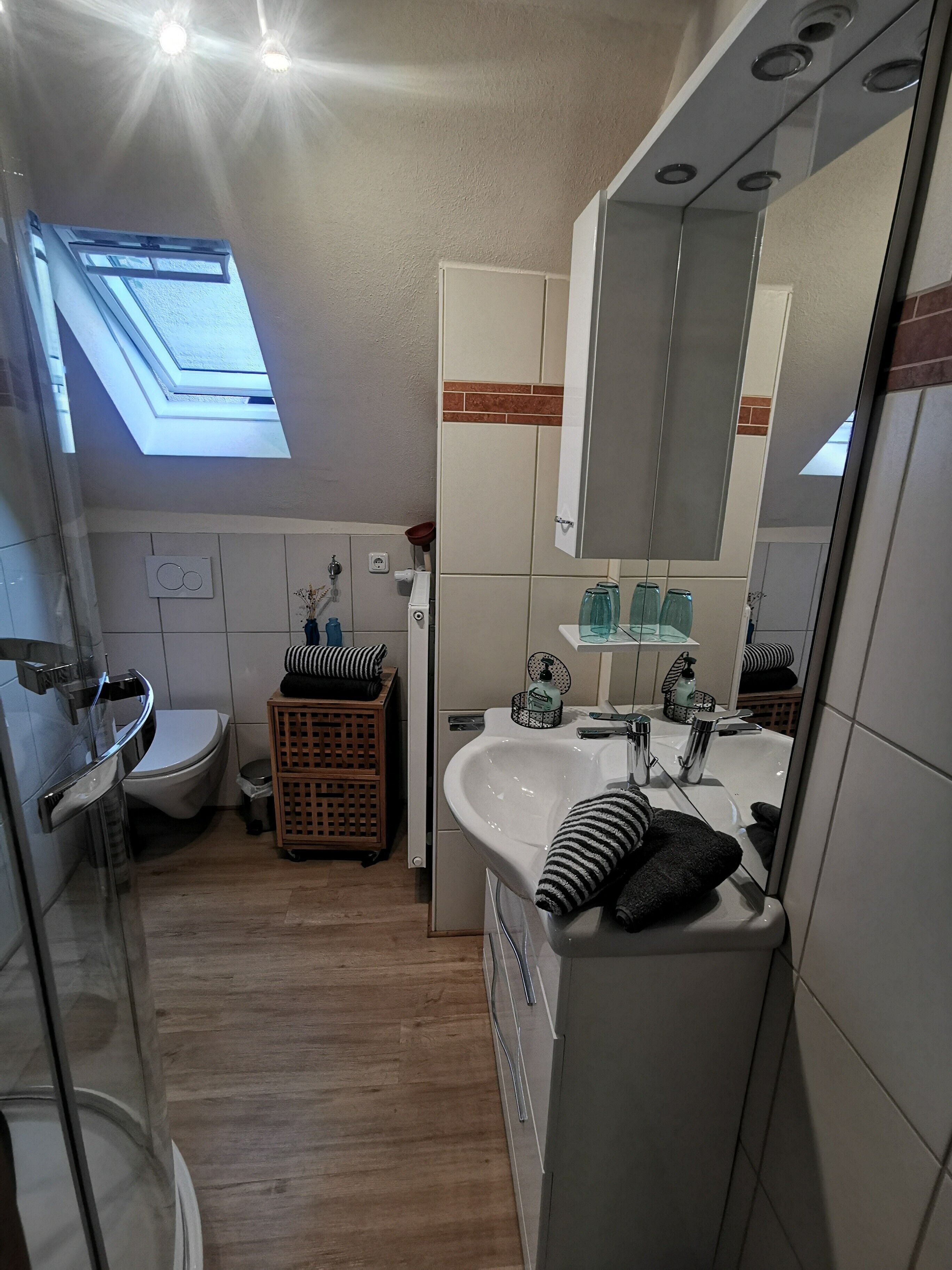 Ein kleines Badezimmer mit Oberlicht, Toilette, Waschbecken mit Spiegel und einer kleinen Holzkiste.