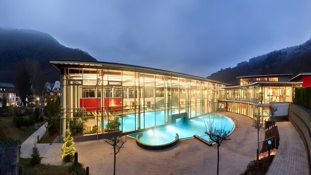 A modern building with a glass facade, a swimming pool, and a mountainous backdrop. - First Floor Vacation Home AusZeit (Bad Bertrich)