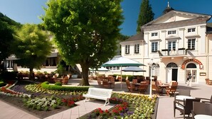 A hotel courtyard with outdoor seating, a large tree, and a building with a classic architectural style. - First Floor Vacation Home AusZeit (Bad Bertrich)