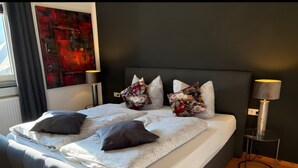 A modern bedroom with a large bed, decorative pillows, a side table, and a floor lamp. - First Floor Vacation Home AusZeit (Bad Bertrich)