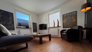 A modern living room with a sofa, a coffee table, a TV, and a painting on the wall. - First Floor Vacation Home AusZeit (Bad Bertrich)
