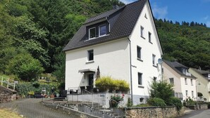 A two-story building with a sloped roof, a balcony with a railing, and a staircase leading to the entrance. - First Floor Vacation Home AusZeit (Bad Bertrich)