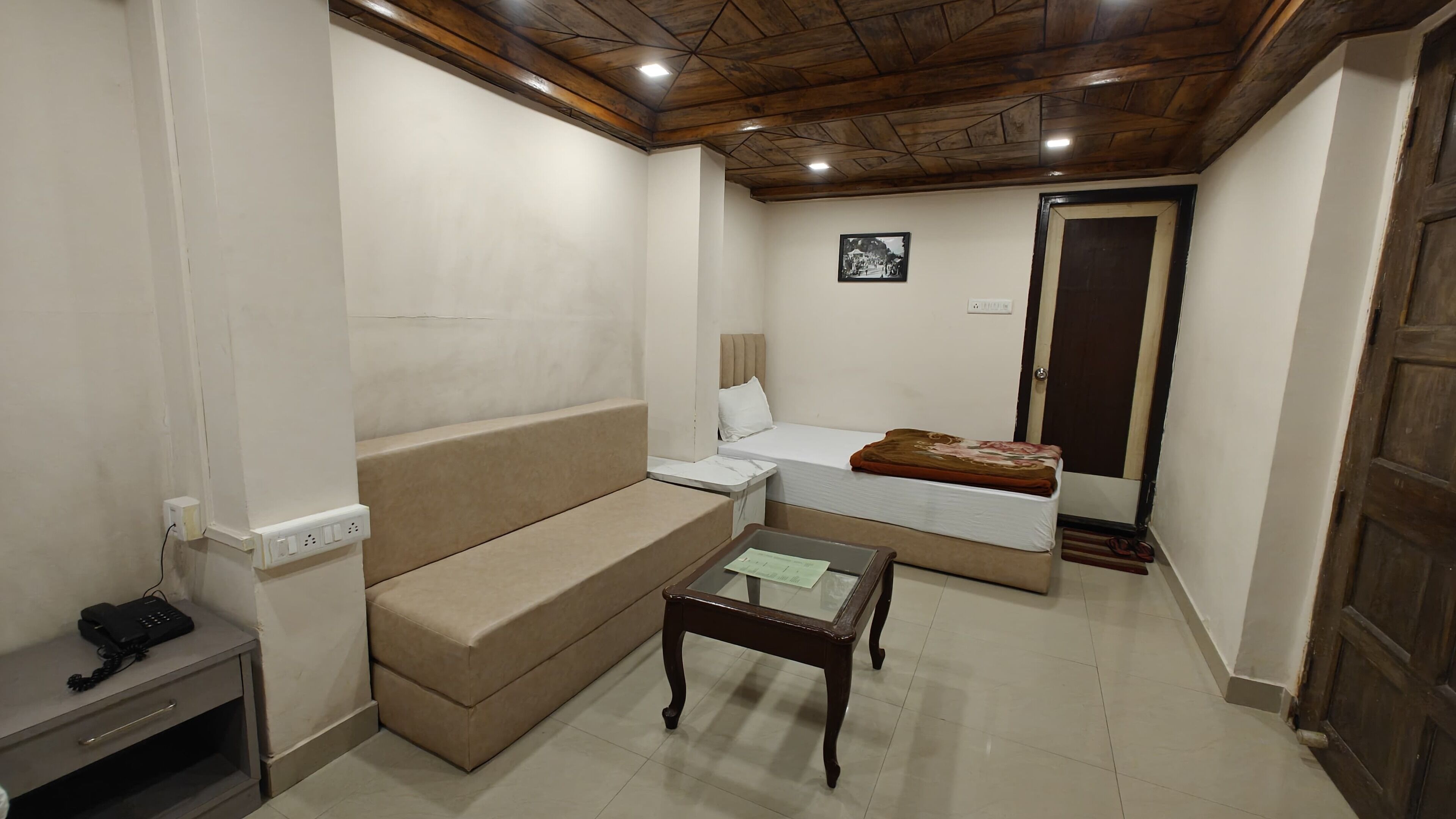 Una stanza compatta con divano, un tavolino, un letto con coperta e una porta in legno.