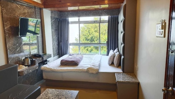 Una camera da letto con un letto, una televisione a parete, una finestra con tende e un tavolino con un bollitore.