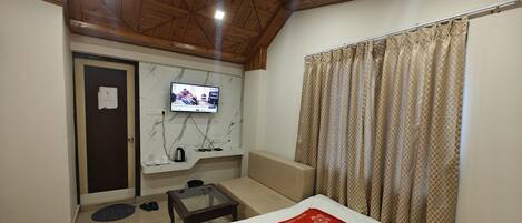 Ein Hotelzimmer mit Bett, Wandfernseher, kleinem Tisch und einer Couch.