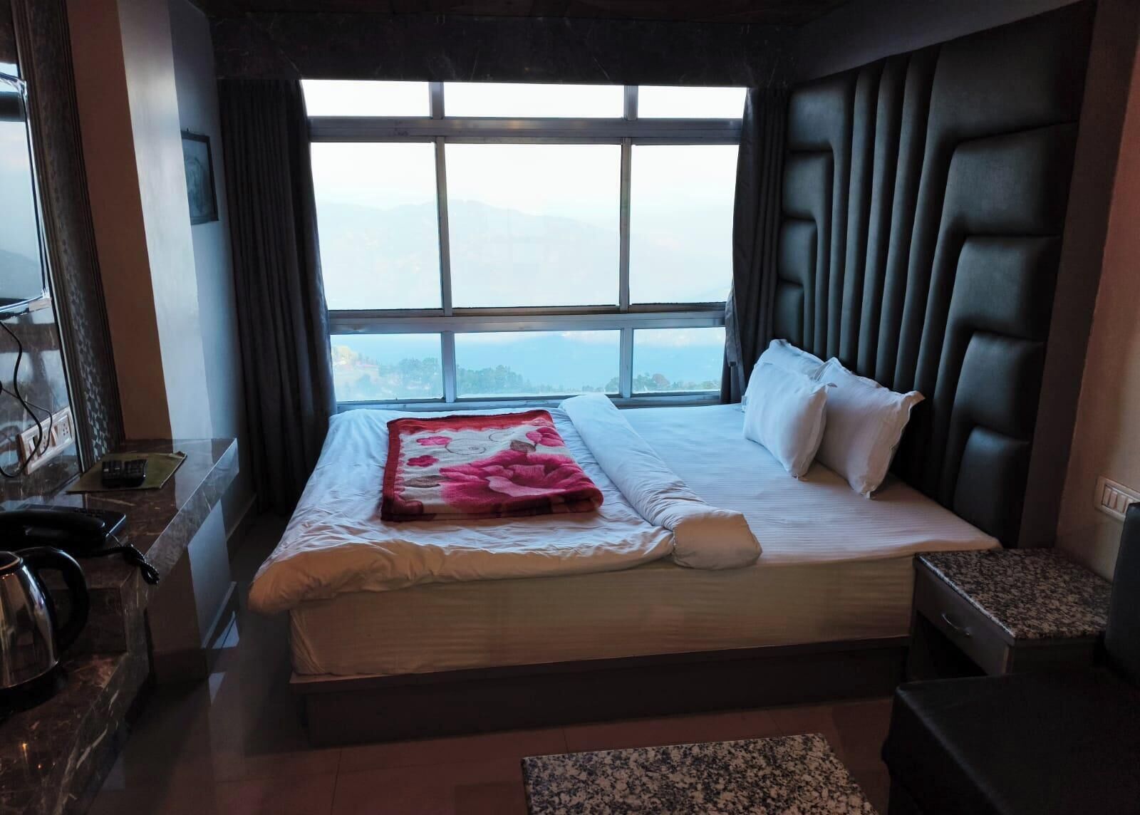 A hotel room with a large bed, a view of the mountains, a small desk, and a chair.