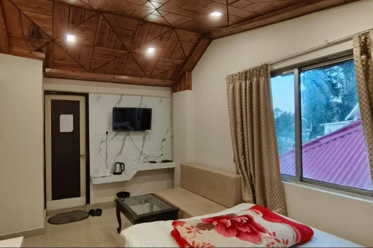 Een slaapkamer met een houten plafond, een televisie aan de muur, een bed met een bloemenprint sprei, een kleine tafel en een raam met gordijnen.