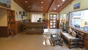 Un'area di accoglienza con una scrivania in legno, un divano e un tavolino. Si vedono piante in vaso e quadri appesi alle pareti.