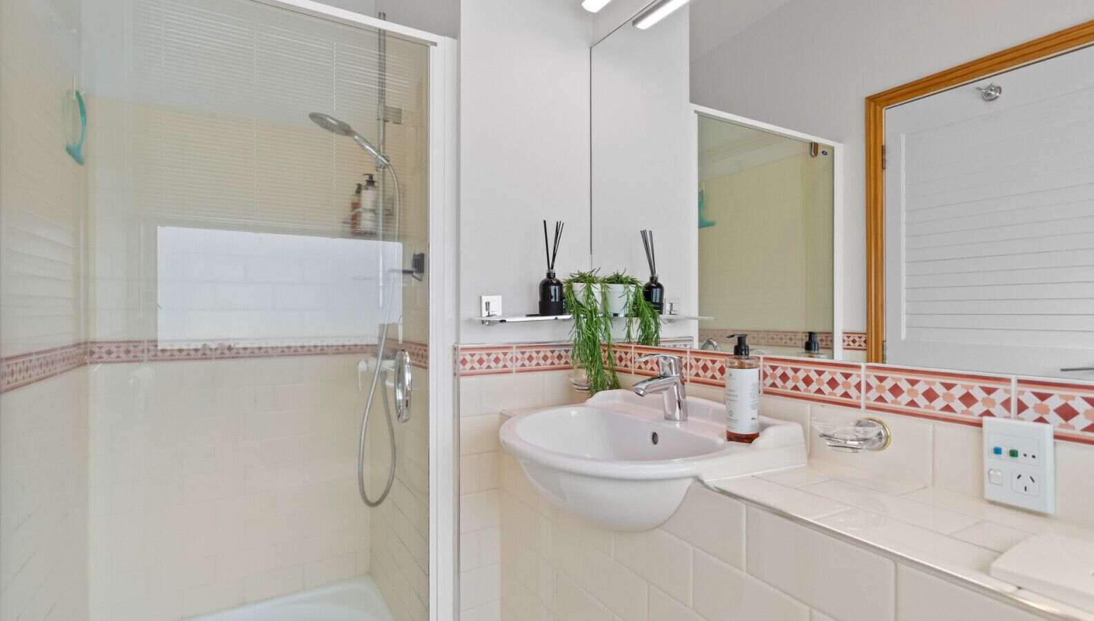 A bathroom with a glass-enclosed shower, a sink with a mirror above it, and a tiled backsplash.