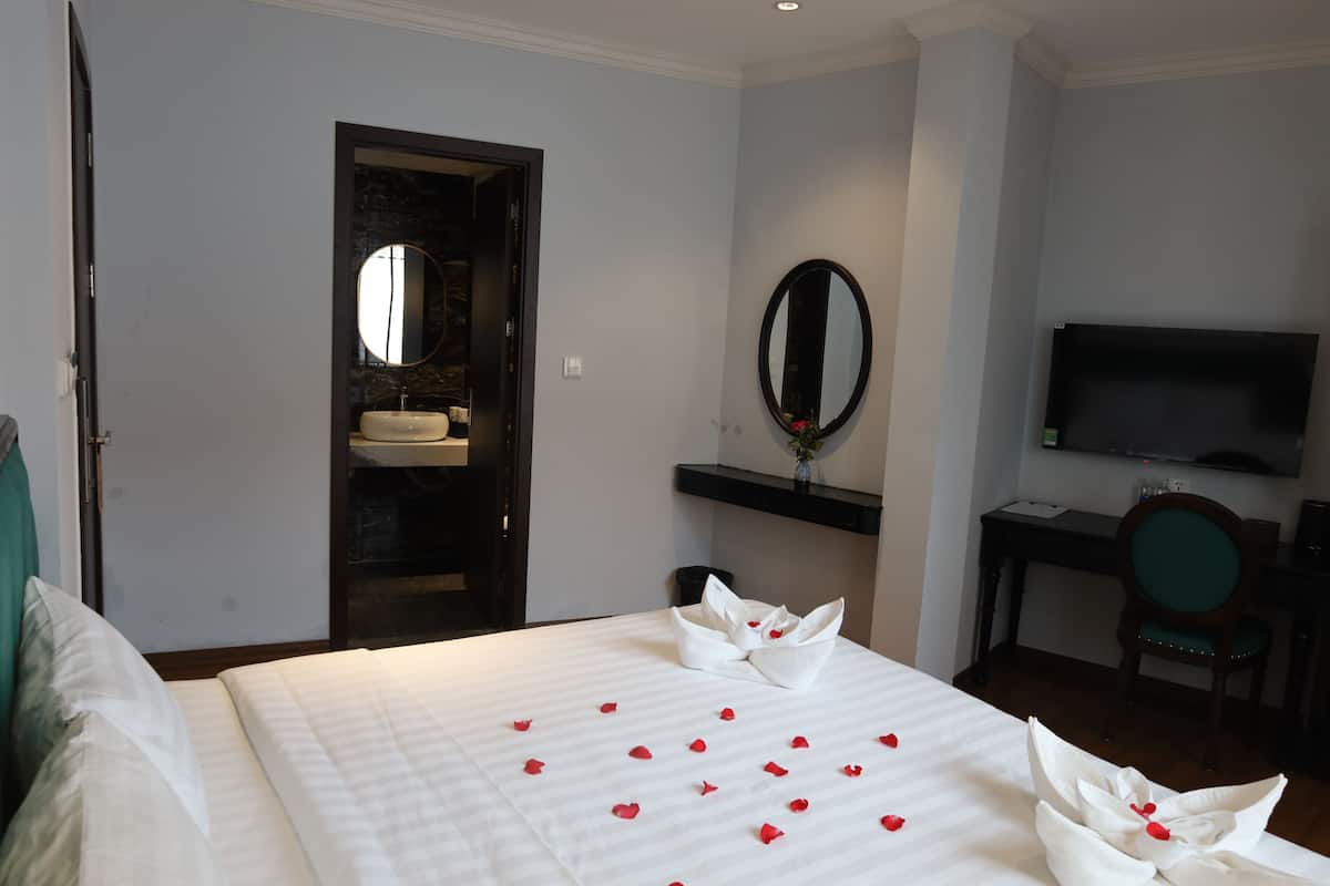 A hotel room with a bed, a bathroom with a sink, a mirror, a desk with a chair, and a television.