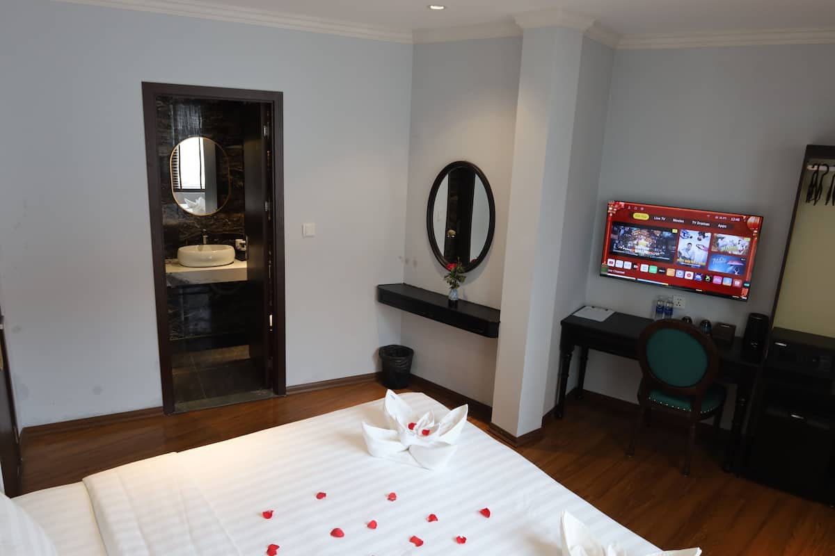 A hotel room with a bed, a desk, a TV, a mirror, and a bathroom.