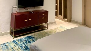 A modern bedroom with a flat-screen TV, a wooden wardrobe, a chandelier, and a large bed. - Sujimoto luxury  (Lagos)