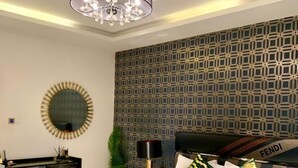 A modern bedroom with a large bed, a desk, a chandelier, and a patterned wall. - Sujimoto luxury  (Lagos)