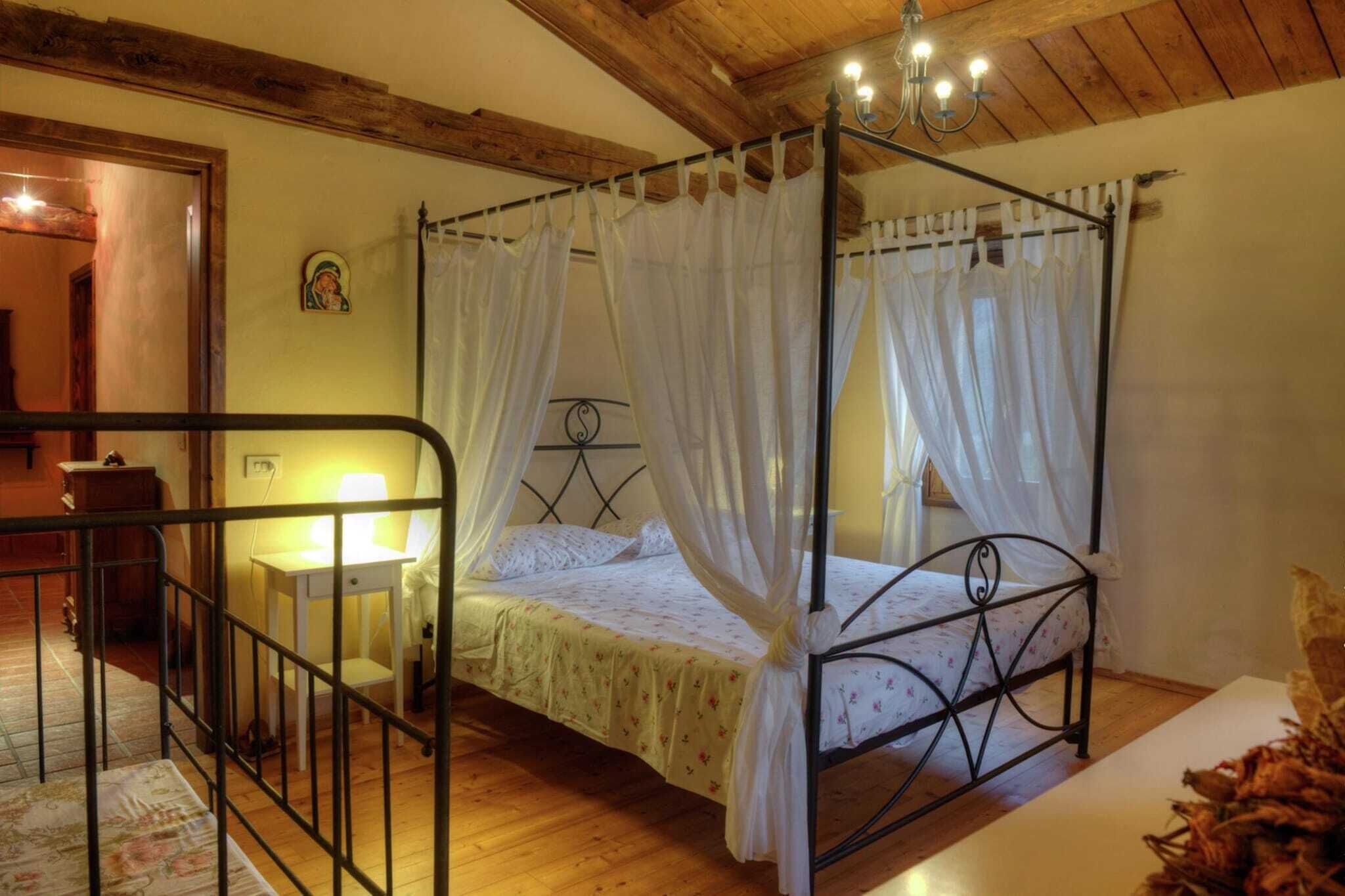 A four-poster bed with white curtains, a bedside table with a lamp, and a wooden ceiling.