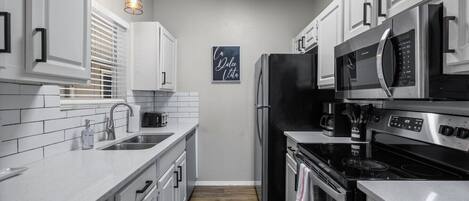 A modern kitchen with white cabinetry, stainless steel appliances, and a wooden floor.