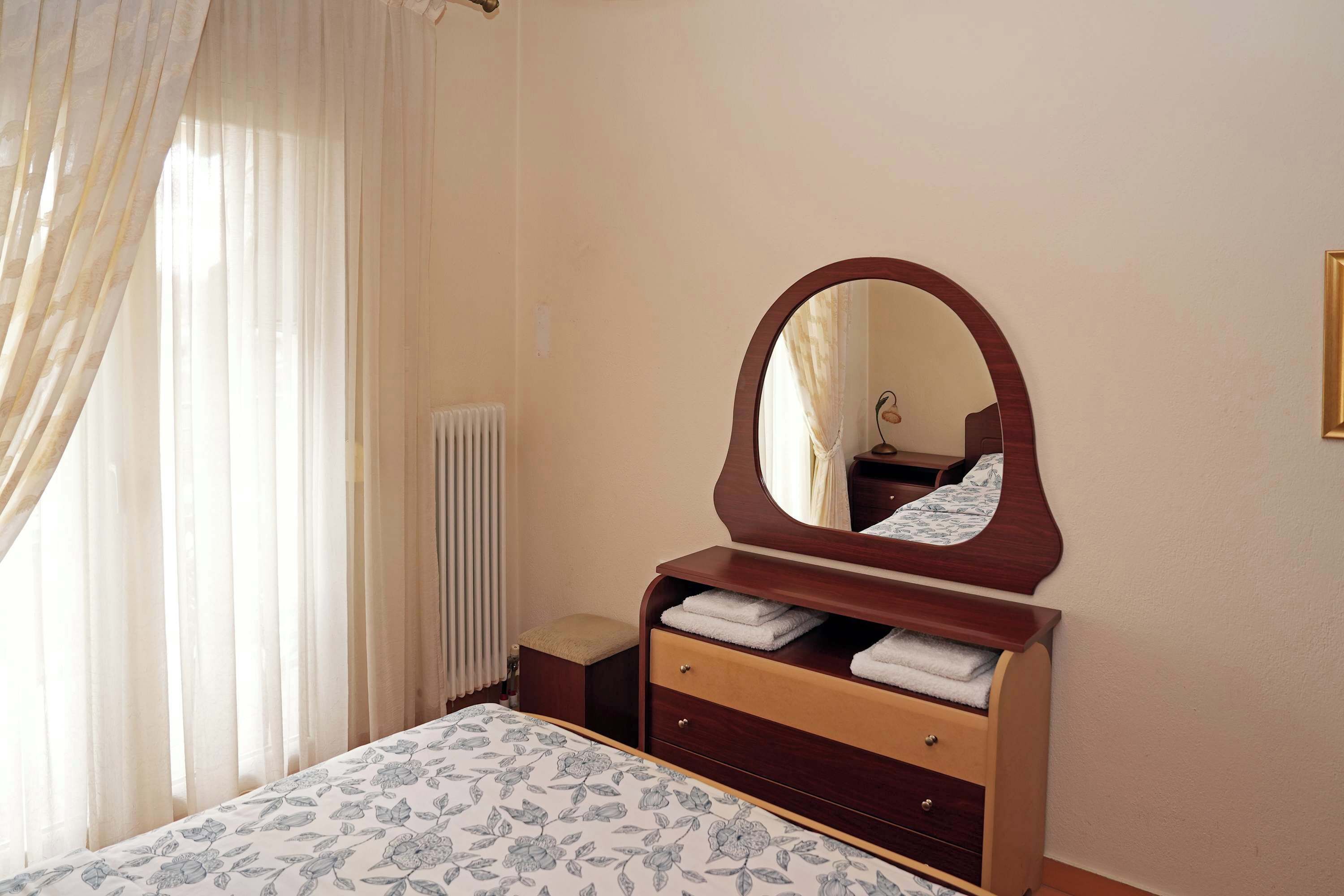A bedroom with a bed, a wooden dresser with a mirror, and a radiator.