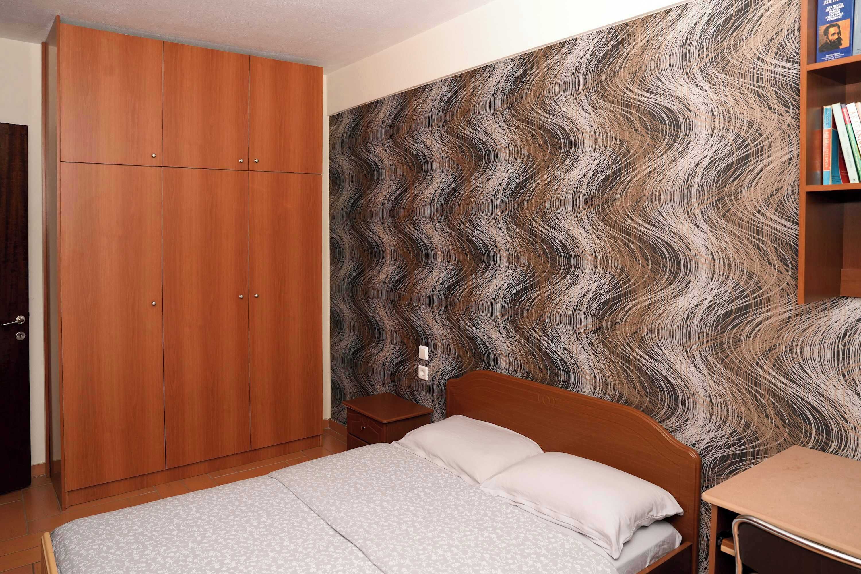 A bedroom with a bed, wooden wardrobe, and a wall with a wavy pattern.