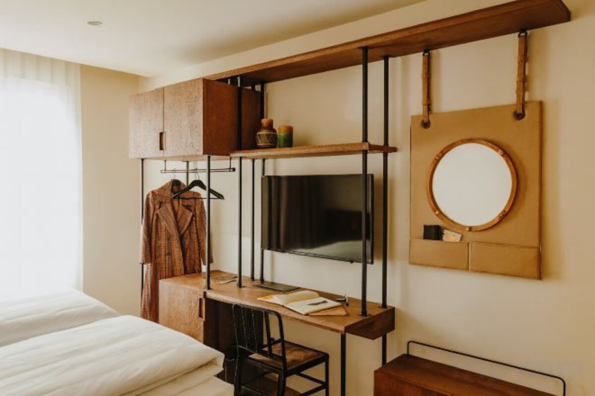 Ein kleines Hotelzimmer mit Bett, Schreibtisch, Stuhl, Fernseher und Spiegel.