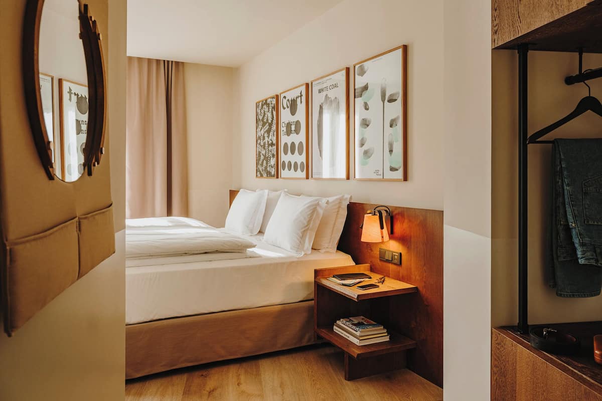 A hotel room with a bed, bedside table, lamp, and framed artwork on the wall.
